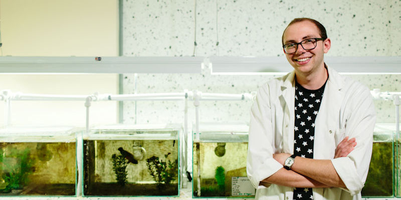 A Biological Sciences student standing in front of fish tanks in a lab.