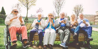 A group of elderly men and women sit on a bench looking at their phones