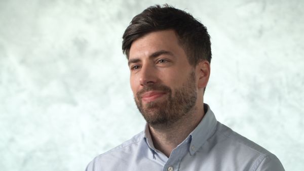 A head and shoulders image of Dr Oliver Price wearing a pale blue shirt in front of a blue-gray background