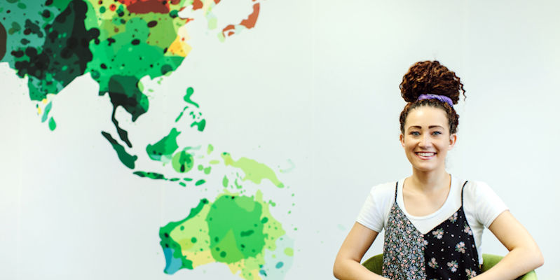 A student standing next to a map of the world.