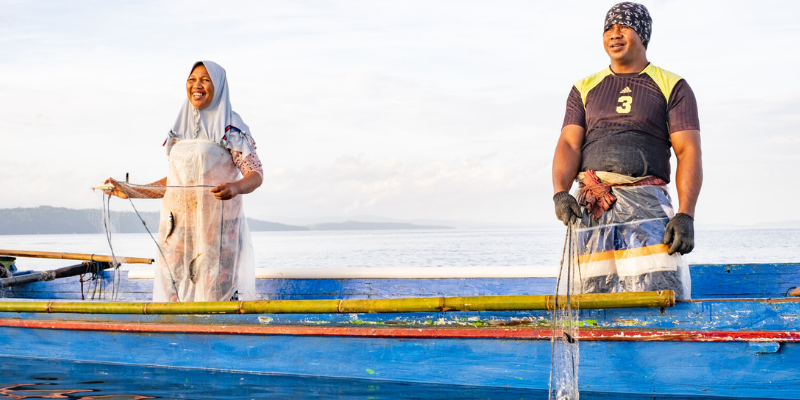A man and woman stand smiling on a small fishing boat.