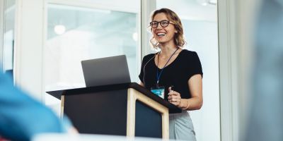 A woman presents behind a podium. She is smiling.