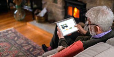 An older man uses a digital tablet on a sofa.