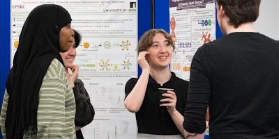 Four people are standing and conversing in front of two scientific posters at an academic or professional event.