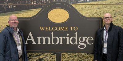 Tim Benton and Stefan Kepinski at The Archers studio, standing in front of a sign that says 'Welcome to Ambridge'