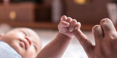 A baby clings onto an adult hand