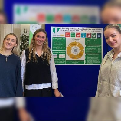 Three University of Leeds students standing in front of a chart that looks at solutions to the challenges of malaria in Nigeria