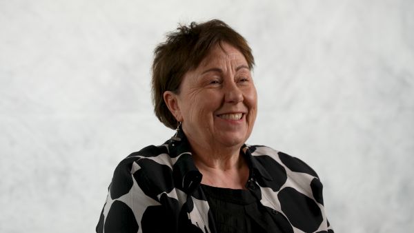 Person in a black-and-white patterned jacket seated against a light grey background, looking slightly to the side.