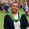 Image of Zhane Murrell-Smith in Leeds University graduation robes outside of the Baines Wing/Great Hall building.