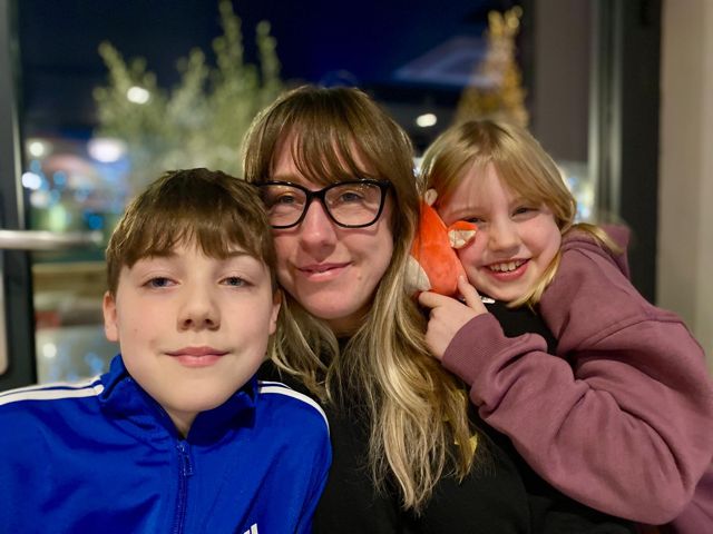 Rebecca smiles at the camera with a young boy and girl.