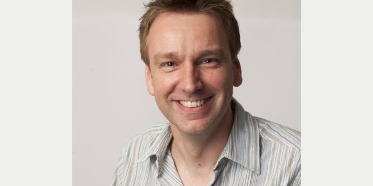 Head-and-shoulders portrait of a person wearing a light striped shirt against a plain light background, facing the camera.