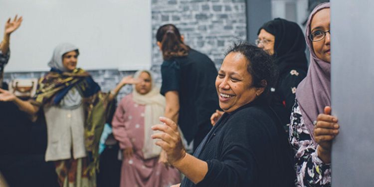 Group of people participating in an indoor movement activity with expressive hand movements.