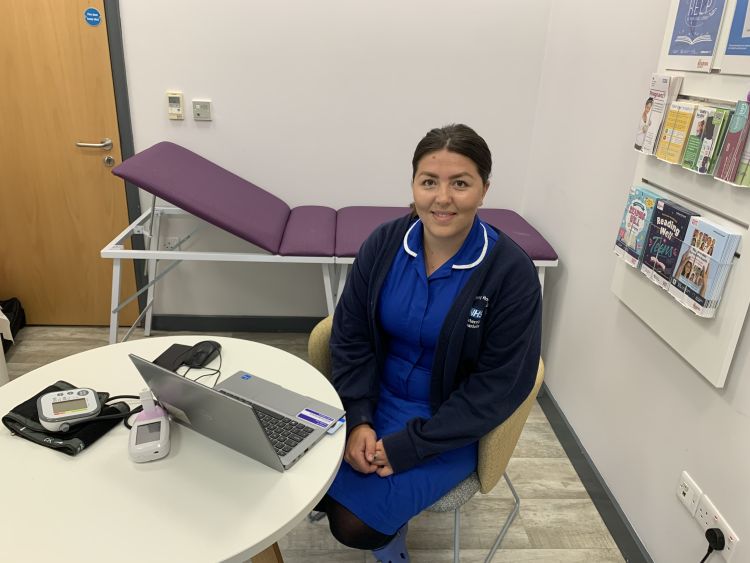 A midwife wearing a blue uniform smiles at the camera. 