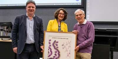Professor Simone Buitendijk and Professor Neil Ranson presenting Dr Richard Henderson with a specially created tapestry inspired by his work in structural biology.